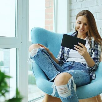 Young happy woman have online video chat using digital tablet computer sitting on balcony in modern loft apartment